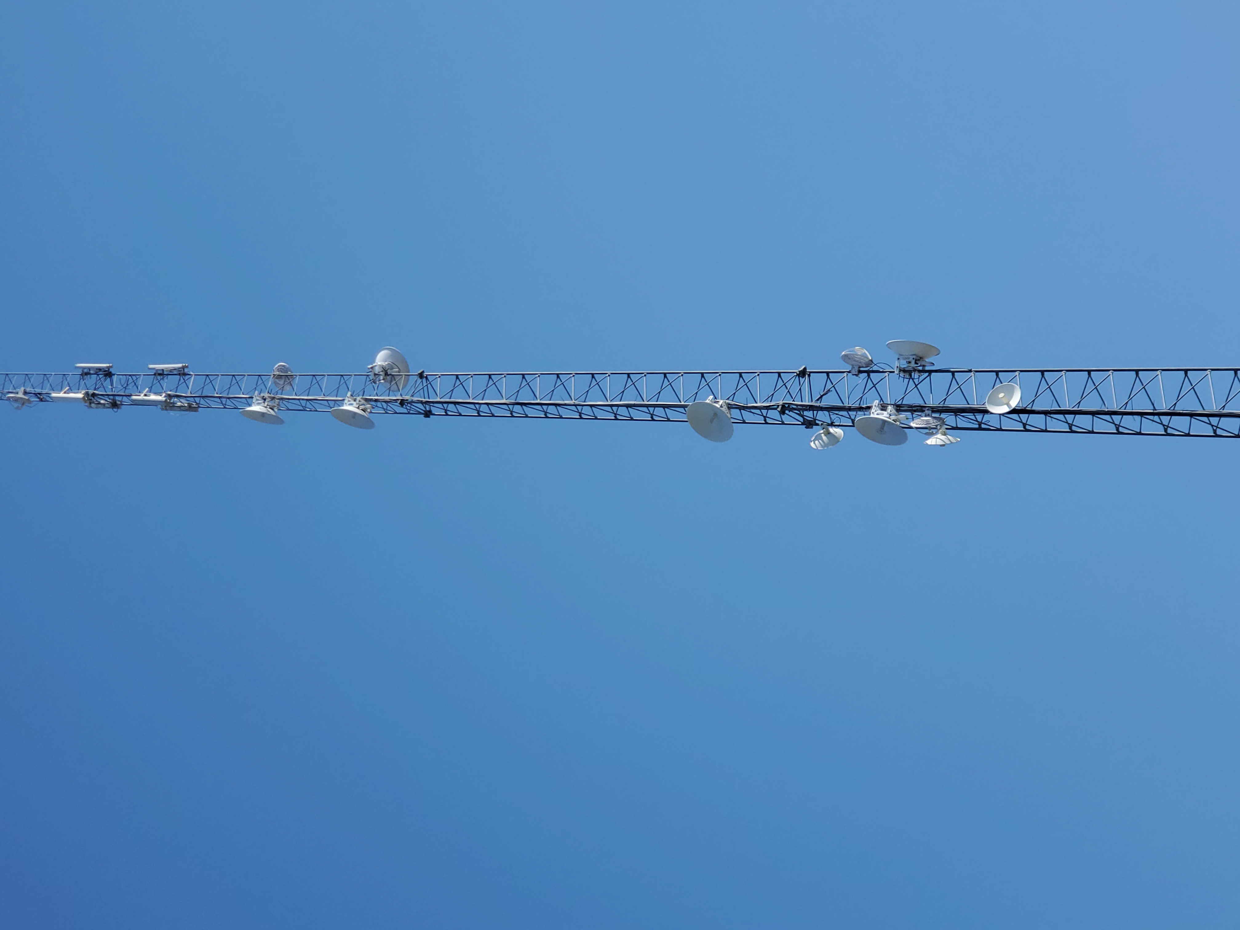 A tall wireless transmission tower with multiple antenna dishes mounted along its height, against a clear blue sky